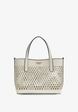 Witte Guess totebag met kruislingse en bloemmotief uitgesneden patronen, twee bovenhandvatten en een gouden logoplaatje aan de voorkant bovenaan.