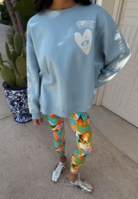 Felpa azzurro chiaro con cuore grafico bianco e scritta "HOPE", abbinata a leggings colorati con motivi vari. Scarpe da ginnastica argento.