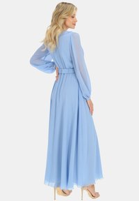 Jasnoniebieska maxi sukienka z długimi przezroczystymi rękawami, marszczonym pasem, zwiewnym dołem i miękką teksturą. Posiada luźny krój i elegancką sylwetkę.