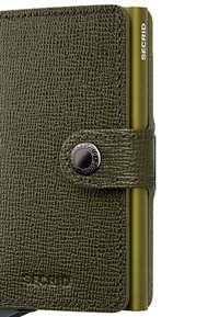 Billetera de cuero texturizado verde con cierre a presión, detalles metálicos y un tarjetero organizado visible en el lateral con la marca 'SECRID'.