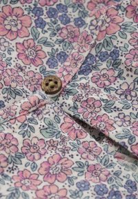 Bloemstof met roze, blauwe en groene patronen, met een houten knoop met donkere gaten, die een getextureerde weving en stikdetail toont.