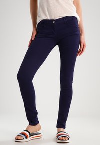 Navy blue slim-fit jeans made of cotton blend with five pockets and a front button closure, paired with multi-striped slide sandals.