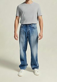 Camiseta gris de cuello redondo combinada con unos vaqueros de mezclilla de corte relajado en azul claro. Detalles desgastados con una textura suave, acentuados por zapatillas blancas.