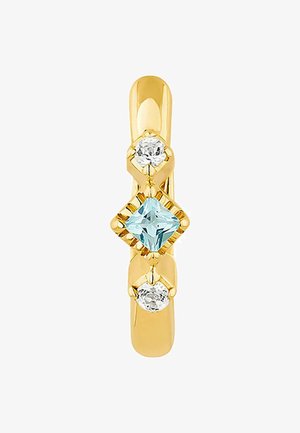 Anillo de oro con tres piedras: una piedra cuadrada azul claro en el centro, flanqueada por dos piedras redondas transparentes, con un acabado pulido.