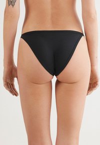 Zwarte bikini onderkant met een lage taille, gladde stof en minimale bedekking. Naaddetails langs de randen.
