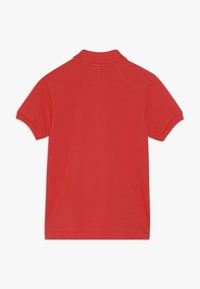 Red polo shirt with a classic collar, short sleeves, and a textured fabric. Back view shows solid color and simple design without patterns.