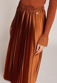Bronzová plisovaná sukně s texturovaným povrchem, s elastickým pasem a dekorativním knoflíkem v pase.