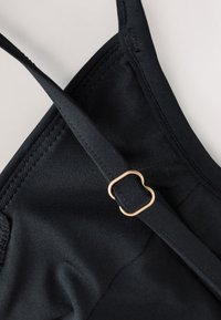 Gros plan d'une sangle noire ajustable avec une boucle dorée sur un vêtement en tissu texturé.