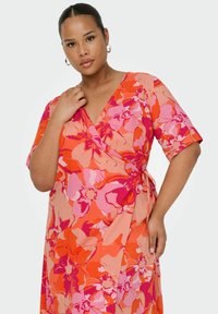 Floral wrap dress featuring vibrant orange and pink colors, short sleeves, and a tie closure at the waist. Soft, lightweight fabric.