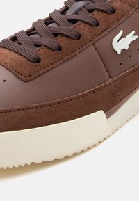 Καφέ αθλητικό παπούτσι με πάνελ από σουέντ και δέρμα, καφέ κορδόνια, λευκή υφασμένη σόλα και λευκό λογότυπο κροκό στα πλευρά.