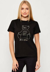 Czarna bawełniana koszulka z nadrukiem misia zdobionego kryształkami, z napisem "GUESS 81" oraz "Unique attitude" poniżej. Krótkie rękawy.