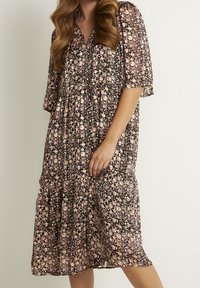 Schwarzes Blumenkleid mit kurzen Ärmeln, das mit rosa und weißen Blumenmustern, einem V-Ausschnitt und einem gestuften Saumdesign versehen ist.