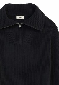 Gilet zippé noir avec une texture côtelée, un large col et un design en forme de V sur la poitrine. Étiquette marquée "RODIER" visible.