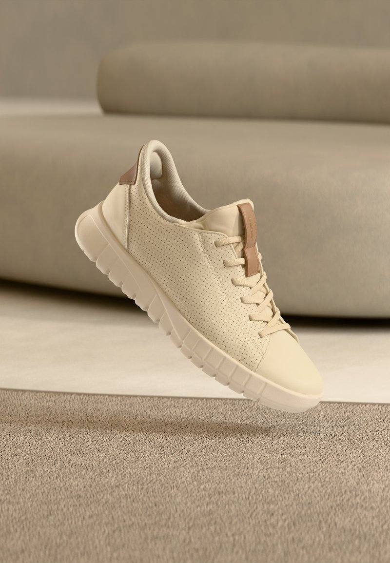 Μπεζ αθλητικό παπούτσι με λείο δερμάτινο φινίρισμα, διάτρητες πλευρές και καφέ λεπτομέρεια στη φτέρνα. Διαθέτει υφή στη σόλα και σχέδιο με κορδόνια.