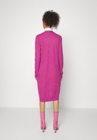 Fuchsia Strickkleid mit langen Ärmeln und geripptem Saum, kombiniert mit knielangen pinken Stiefeletten mit Absatz. Glatte Textur, schlichtes Design.