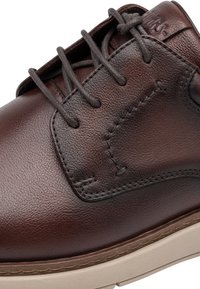 Gros plan d'une chaussure en cuir marron à lacets avec des coutures détaillées et une semelle en caoutchouc beige.