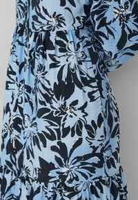 Abito floreale blu con grandi fiori neri e bianchi, caratterizzato da un design a strati e realizzato in un tessuto leggero e testurizzato.