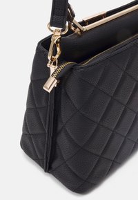 Zwarte leren handtas met een doorgestikt patroon en gouden ritssluitingdetails. Voorzien van een handvat met gouden beslag en een gestructureerde vorm.