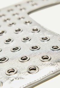 Metallisk sølvmateriale med et mønster af jævnt fordelte, cirkulære metaløjer. Glat struktur med en blank finish.