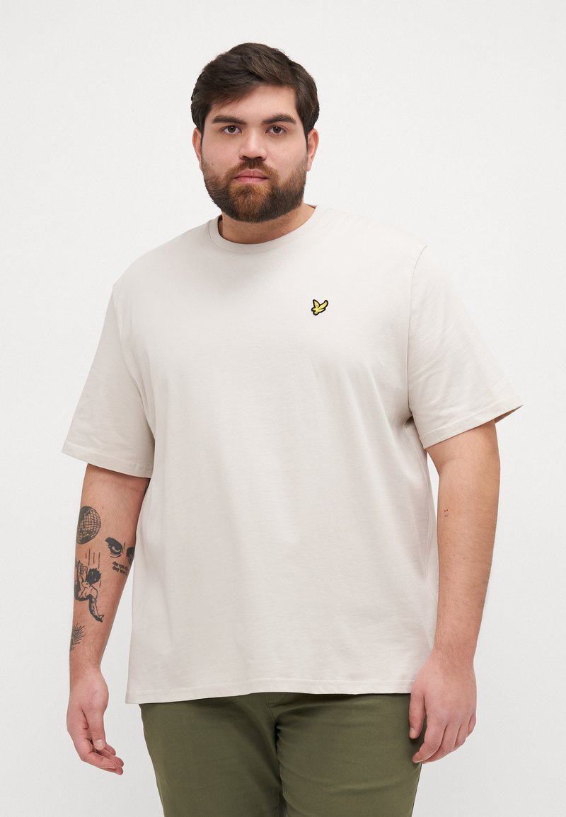T-shirt beige clair à manches courtes avec un petit logo brodé jaune sur la poitrine, fabriqué en tissu coton doux.