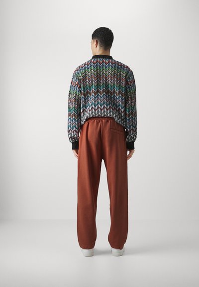 Mitmevärviline  zigzag-mustriga bomber-jakk musta kaelusega, koos rost-pruunide dressipükste ja valgete tossudega.