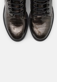 Botas de cuero oscuras y brillantes con un patrón de cocodrilo, con cordones negros y una suela negra texturizada, vistas desde arriba.