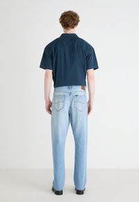 Maglietta a maniche corte, blu navy, con vestibilità comoda, abbinata a jeans azzurri chiari e larghi. Tessuto testurizzato e dettagli di cucitura minimi visibili.