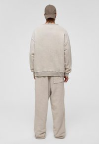 Beige oversized sweatshirt met geribbelde manchetten, gecombineerd met bijpassende loszittende broek met een achterzak. Persoon draagt een tan-kleurige pet.