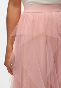 Gonna in tulle rosa chiaro con volant a strati, dotata di un ampia fascia in vita. Il tessuto ha una texture morbida e trasparente che crea una silhouette fluida.