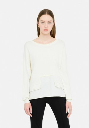 Maglione giallo chiaro a maniche lunghe con pannello frontale testurizzato, scollatura rotonda e due tasche frontali. Abbinato a pantaloni neri aderenti.