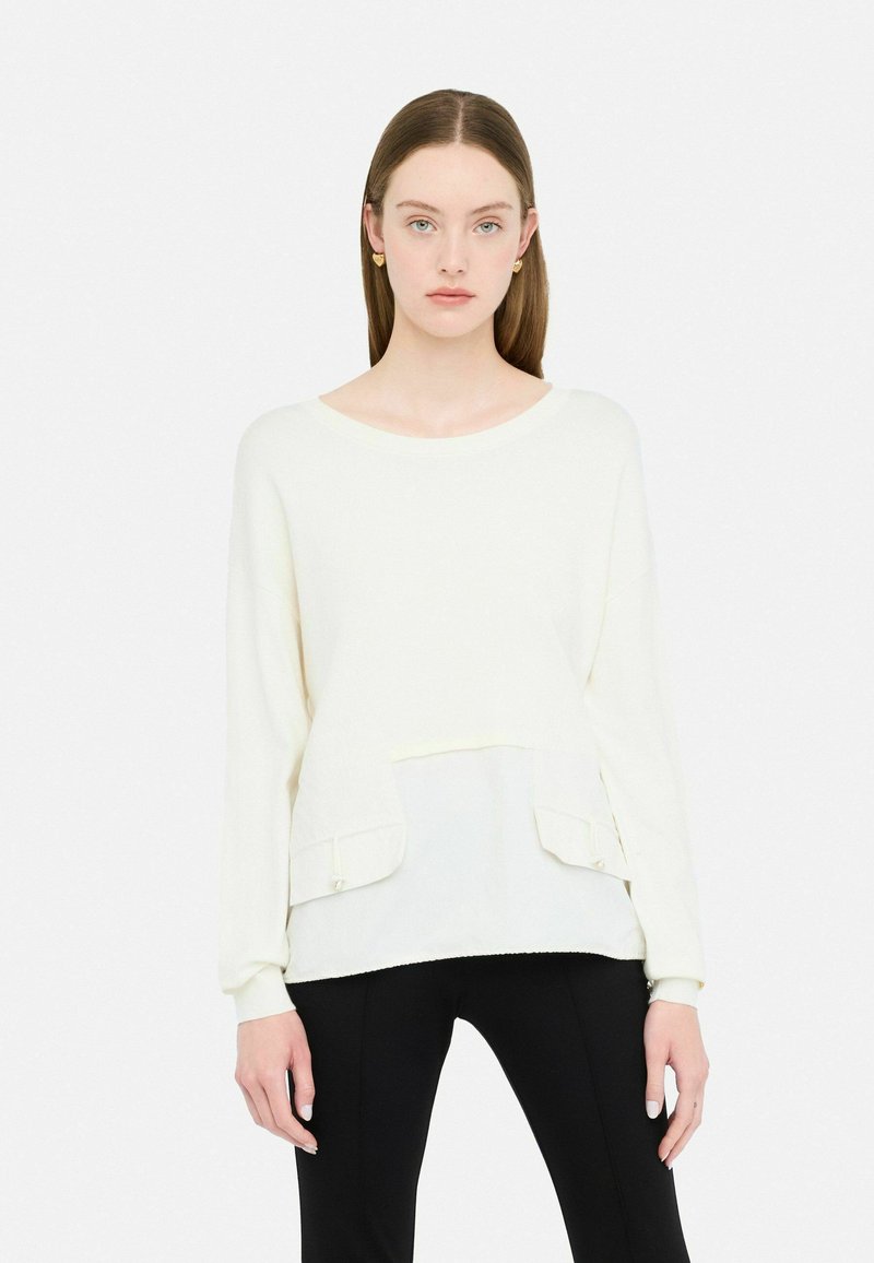 Maglione giallo chiaro a maniche lunghe con pannello frontale testurizzato, scollatura rotonda e due tasche frontali. Abbinato a pantaloni neri aderenti.