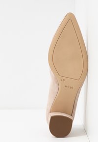Semelle de chaussure beige à bout pointu, taille 4½ et marque Högl, reposant à la verticale contre un mur blanc.