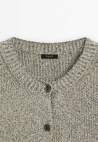 Cardigan en maille gris et noir avec col côtelé et deux boutons noirs, montrant la partie supérieure de la poitrine et le décolleté.