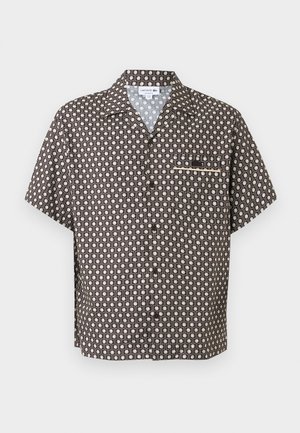 Camisa de manga corta con botones, con patrón geométrico en blanco y negro y bolsillo en el pecho, diseñada por Lacoste.