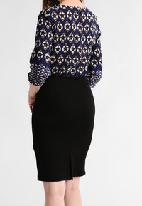 Completo a due pezzi composto da una blusa a maniche lunghe blu e bianca a fantasia e una gonna a tubino nera aderente con spacco sul retro.