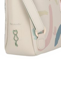 Hellbeige Handtasche aus strukturiertem Kunstleder, mit pastellfarbenen abstrakten Mustern und einem grünen katzenförmigen Akzent.