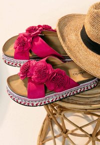 Fuchsia Plattform-Sandalen mit floralen Akzenten, aus Wildleder, mit strukturiertem Sohle und dekorativen geflochtenen Details. Neben einem Strohhut.