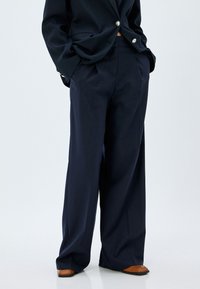 Pantalones a rayas en azul marino con un diseño de pierna ancha, confeccionados en una tela suave. Presentan una cintura alta y bolsillos laterales.