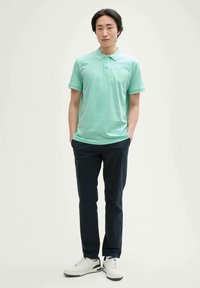 Ljusgrön polo skjorta med korta ärmar och krage, ihop med marinblå byxor och vita sneakers. Slät textur, minimal varumärkeslogotyp på skjortan.