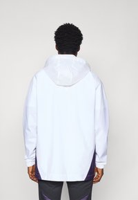 White jacket with a hood, featuring purple accents at the bottom. Loose fit, elastic cuffs, and a smooth, lightweight texture.