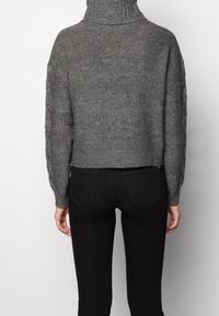 Suéter gris de punto grueso con cuello alto, mangas largas y dobladillo acanalado, combinado con pantalones negros ajustados. Diseño casual y cropped.