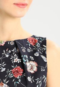 Blommig klänning med en mörk marin bakgrund som pryds av röda och rosa blommor, gröna blad och vita detaljer; mjukt tyg, strukturerad design.