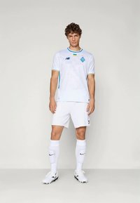 Balta futbola krekls ar gaiši zili akcentiem, ar logo uz krūtīm, kombinēts ar baltām šortiem un zeķēm; izstrādāts sportiskai veiktspējai.