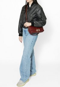 Veste en cuir marron type bombardier, jeans évasés bleu clair et sneakers crème. Un petit sac bandoulière rouge avec des accents en métal argenté.