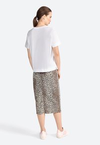 Witte t-shirt met korte mouwen gecombineerd met een knielange rok met luipaardprint en lichtroze sneakers. Glad stof, casual pasvorm en dierenpatroon.