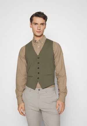 Gilet vert olive avec un col en V, cinq boutons noirs et deux poches à l'avant, porté sur une chemise beige, associé à un pantalon gris clair.