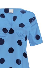 Robe courte en satin bleu à manches courtes avec de grands pois noirs et un décolleté en V, montrant la partie supérieure avant et la zone des épaules.