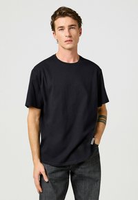 Sort bomulds T-shirt med rund hals, korte ærmer og en afslappet pasform. Bemærkelsesværdigt sideetiket og glat tekstur. Sammen med mørke jeans.