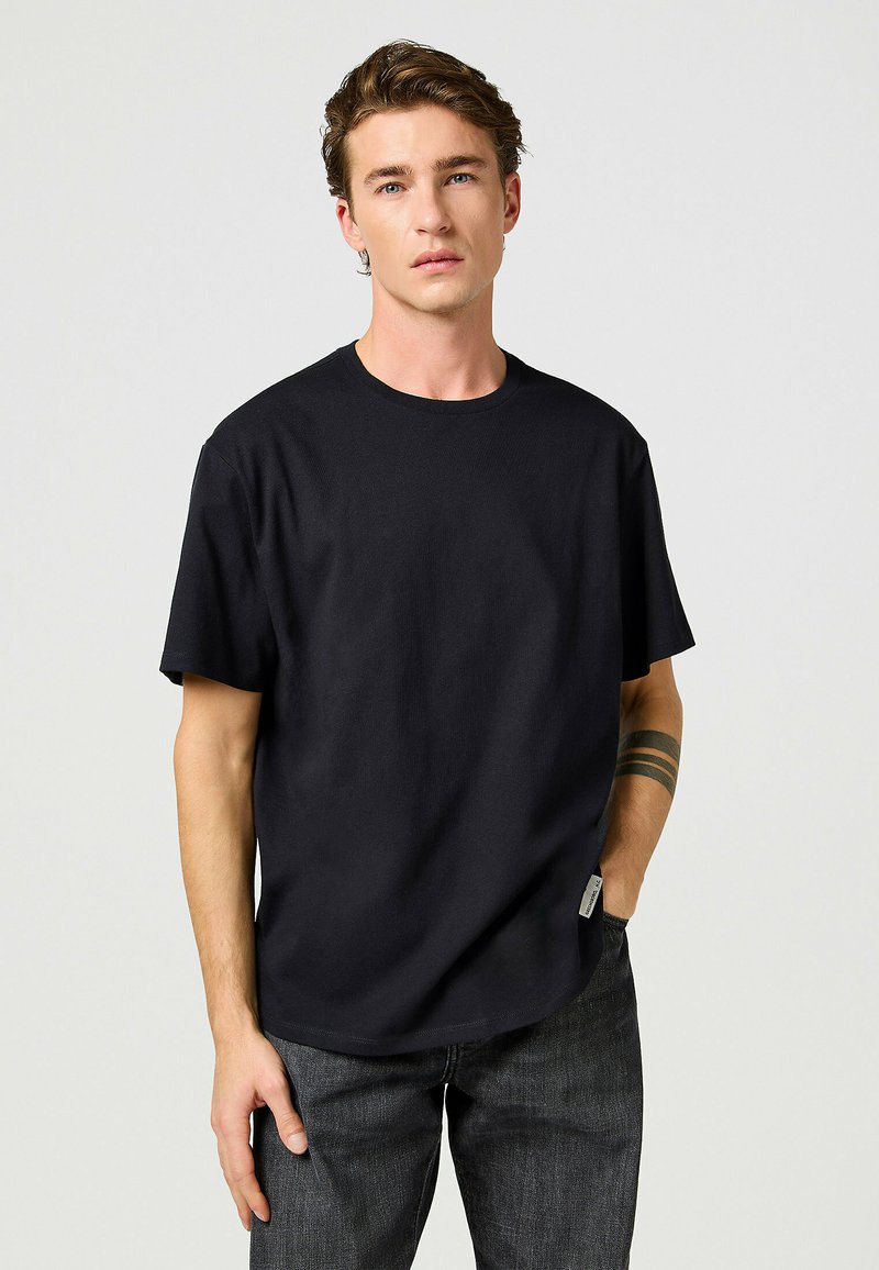 Sort bomulds T-shirt med rund hals, korte ærmer og en afslappet pasform. Bemærkelsesværdigt sideetiket og glat tekstur. Sammen med mørke jeans.