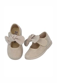 Zapatos infantiles de ante beige con punta redondeada, un gran lazo en la parte delantera y una correa de Velcro. Suela de goma plana y forro interior suave.
